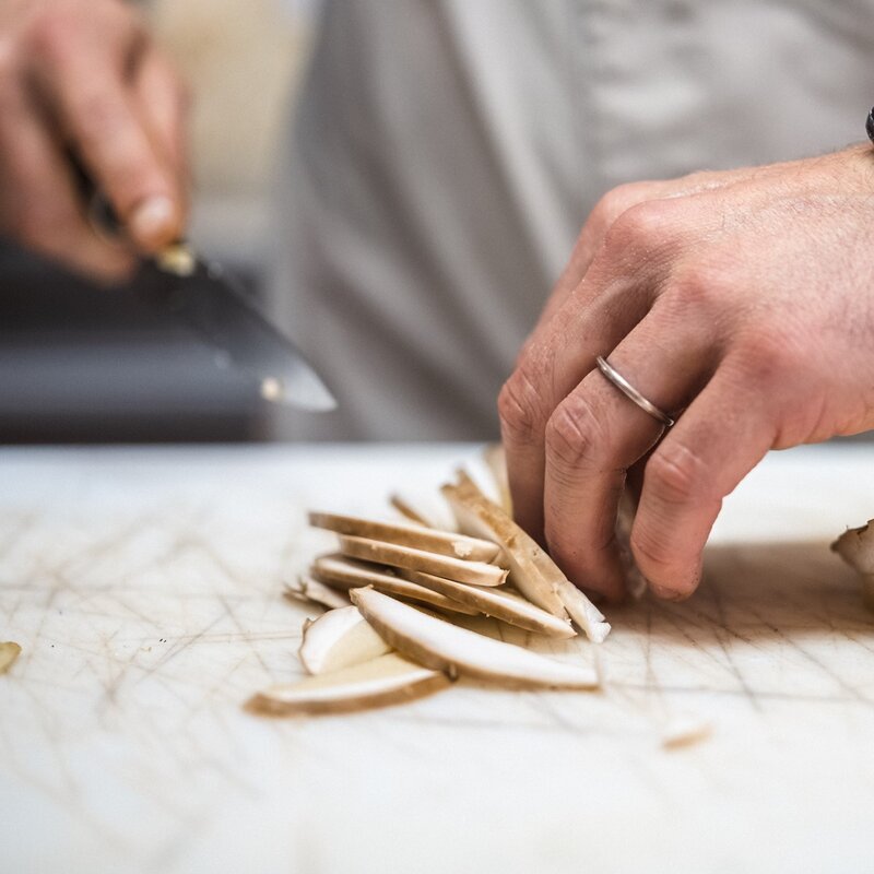 Primo piano delle mani di uno chef impegnato nella preparazione dei funghi | © Frame&Work, 2024