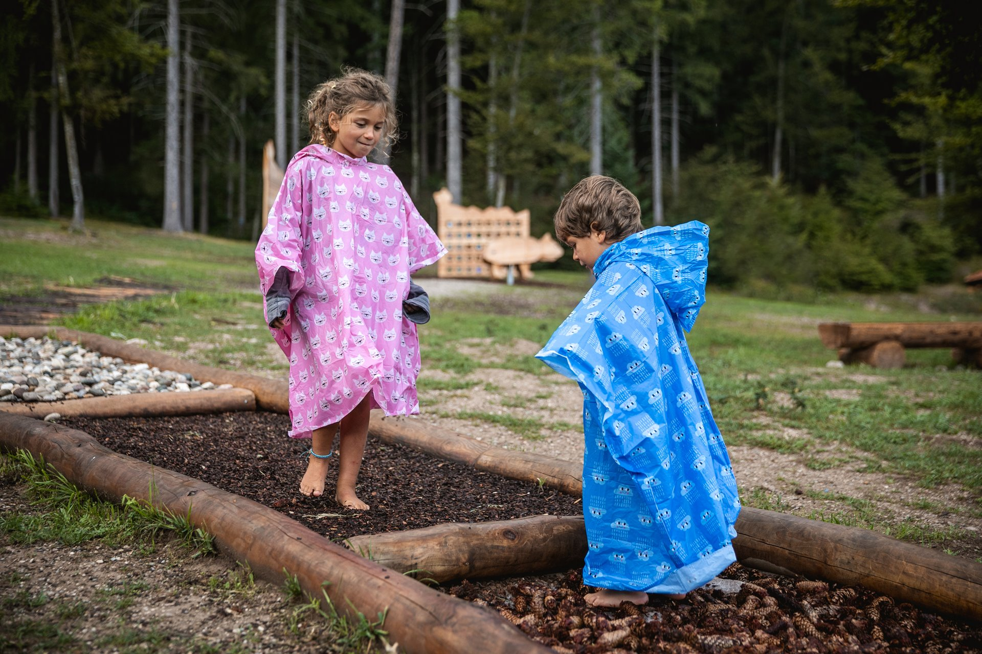 Bambini giocano sul sentiero didattico del Sarnacli Mountain Park di Andalo indossando un impermeabile per la pioggia. | © Oliver Astrologo, 2019