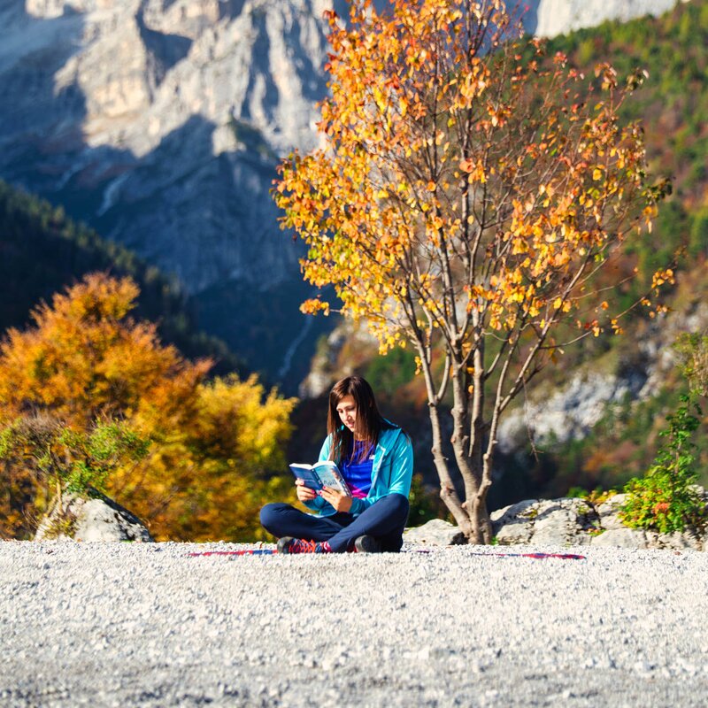 Ragazza seduta sulla riva del lago di Molveno con alle spalle le Dolomiti di Brenta legge un libro | © Filippo Frizzera, 2020