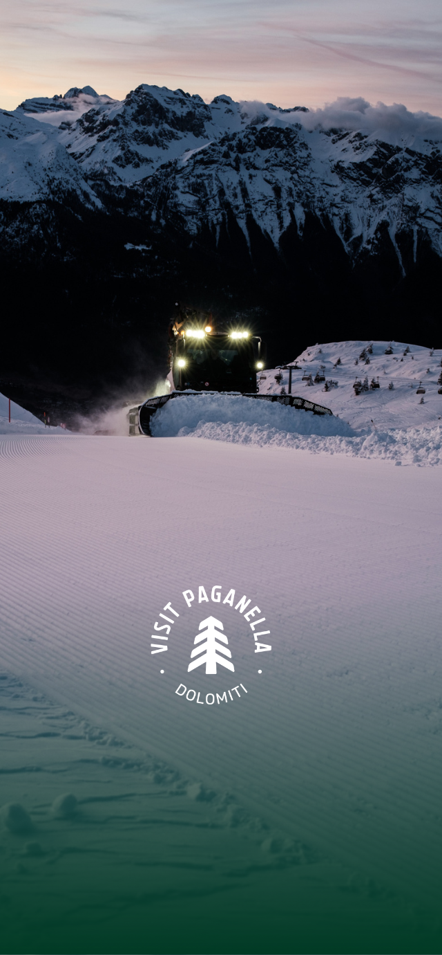 nell'immagine: all'alba un gatto delle nevi tira la pista con le Dolomiti di Brenta sullo sfondo. im text: Was ein Pistenraupenfahrer macht | © Frame & Work, 2024