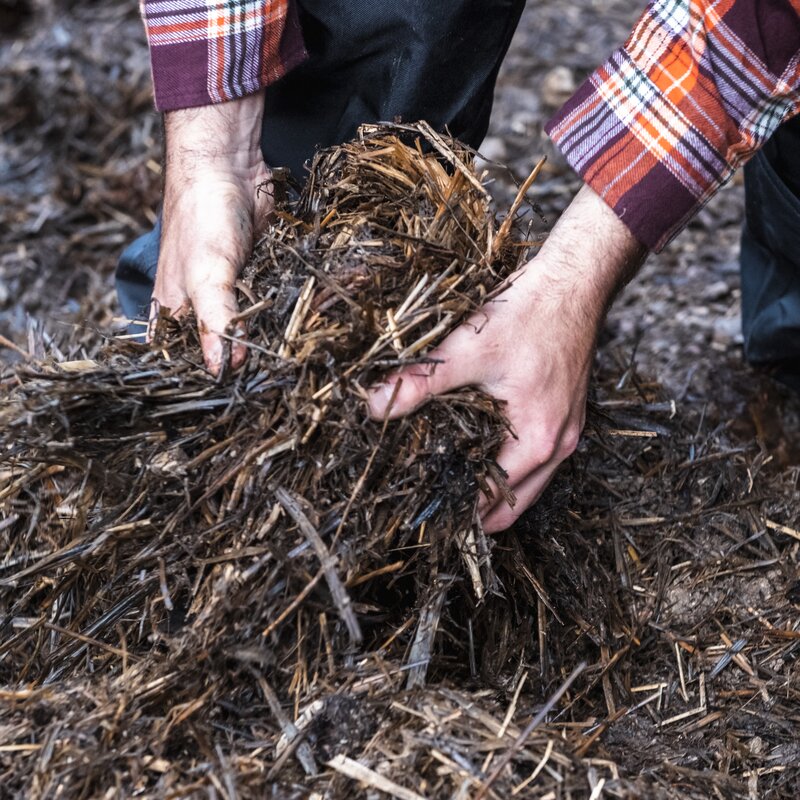 Hands of a trail builder arranging hay and dry wood on the path of one of the trails in the Dolomiti Paganella Bike Park | © Frame & Work, 2022