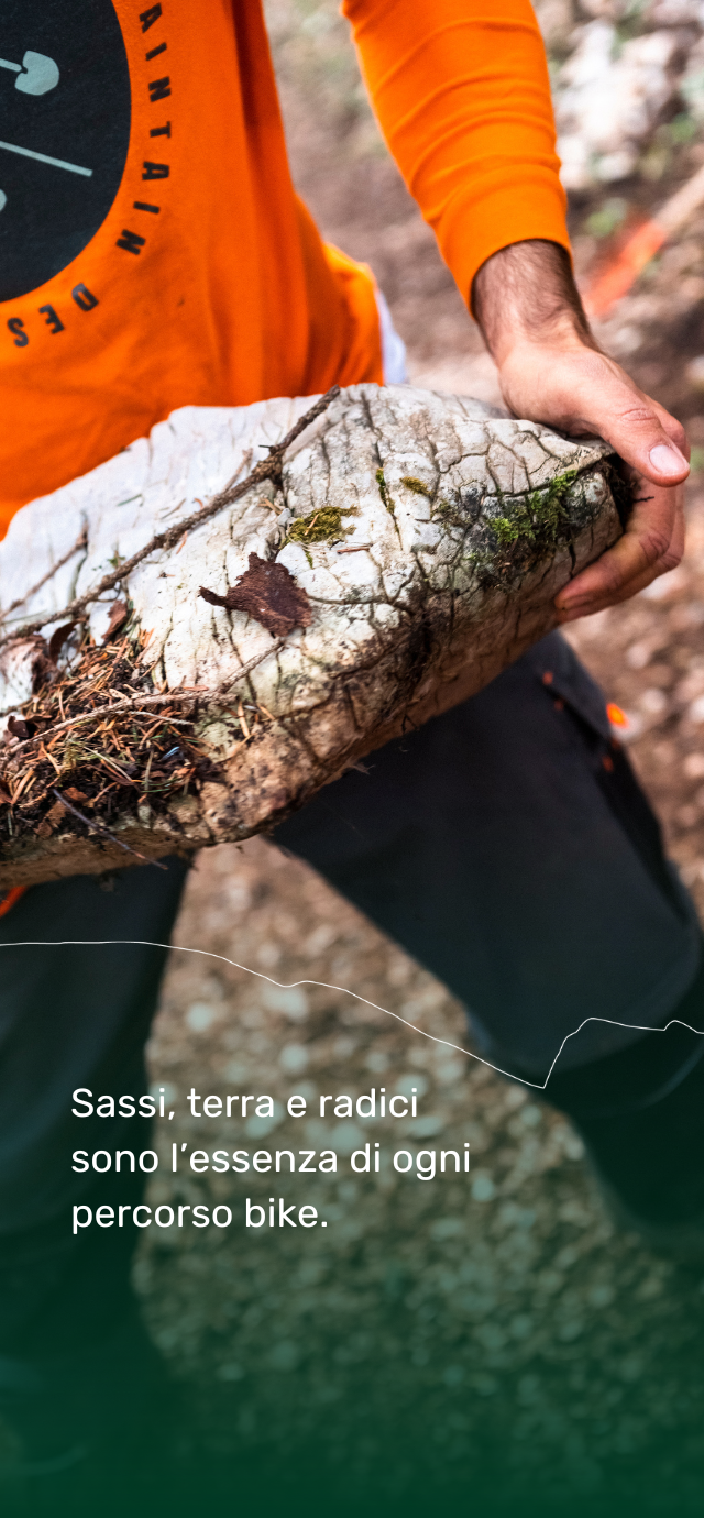 Nell'immagine: un trailbuilder tiene tra le mani un grande masso entratto dal fondo del trail di mountain bike. Nel testo: sassi, terra e radici sono l'essenza di ogni percorso bike. | © Frame & Work, 2024