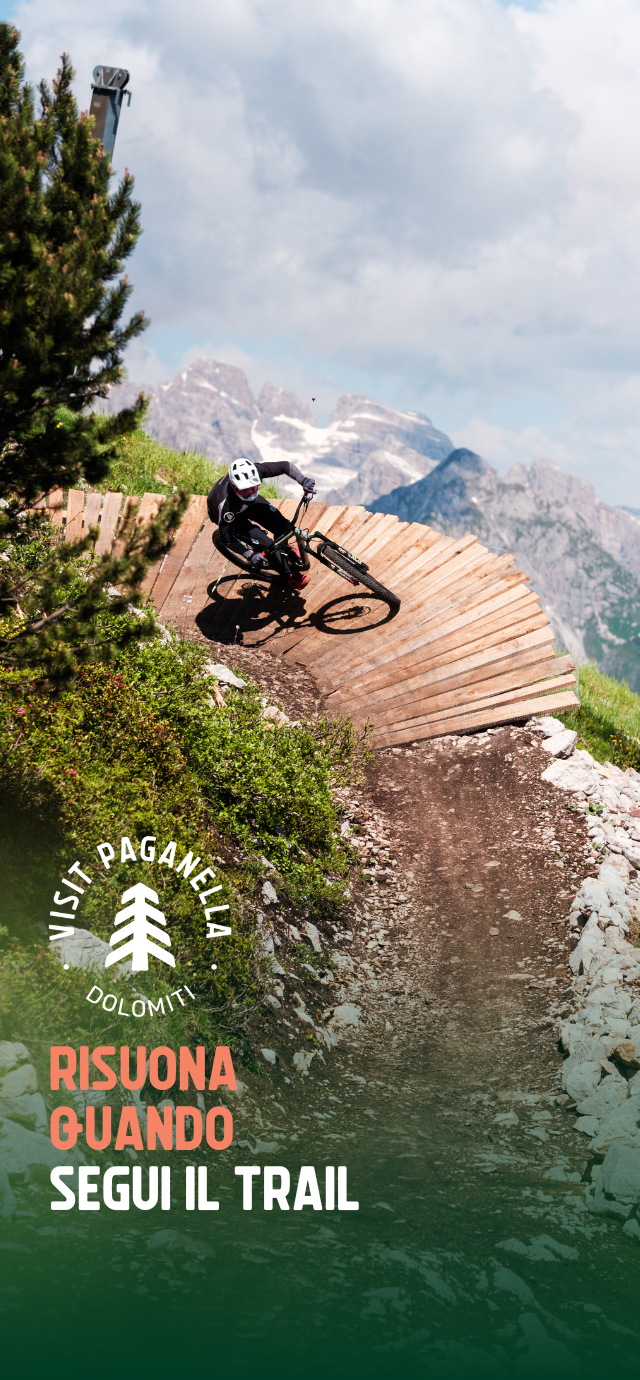 Nell'immagine: un biker percorre un wallride, sullo sfondo la vista delle Dolomiti di Brenta. Nel testo: Risuona quando segui un trail. | © Filippo Frizzera, 2024