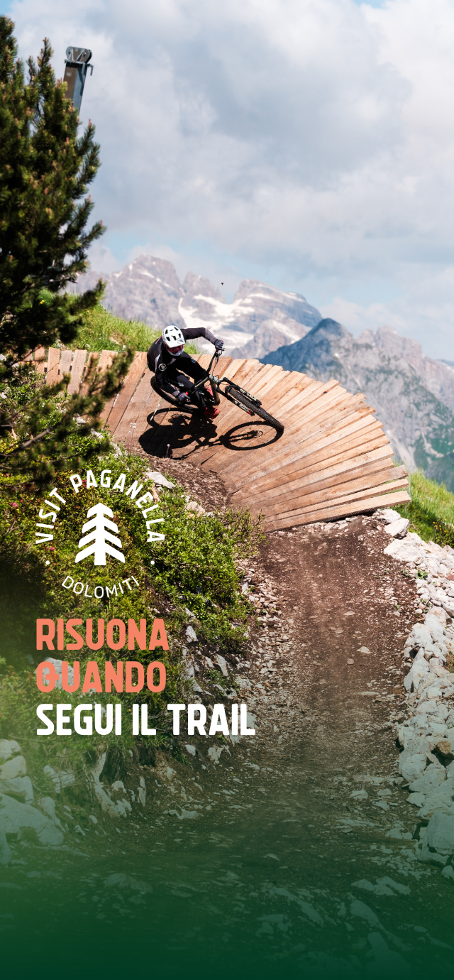 Nell'immagine: un biker percorre un wallride, sullo sfondo la vista delle Dolomiti di Brenta. Nel testo: Risuona quando segui un trail. | © Filippo Frizzera, 2024