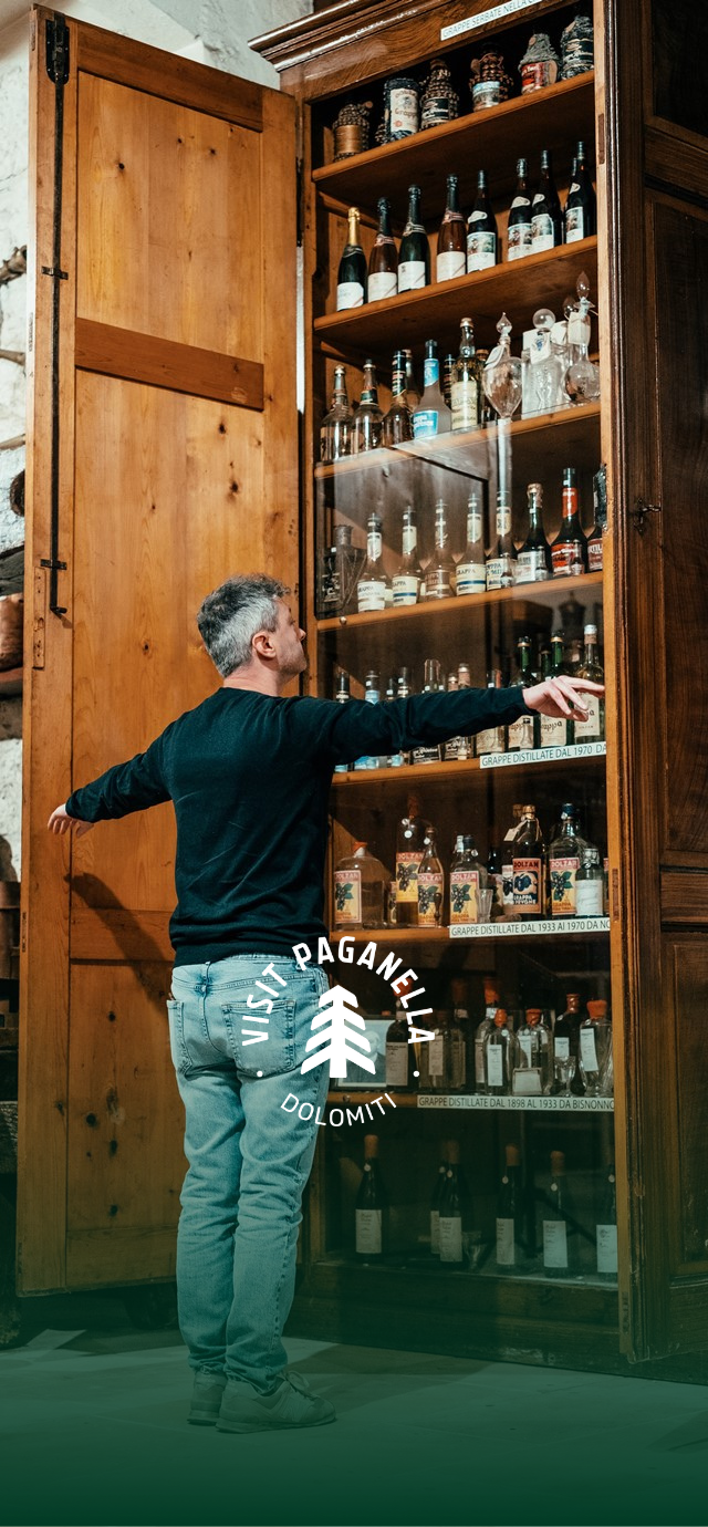 In the image: Mauro opens his pantry full of his company's historic grappas. In the text: Discover our story. | © Frame & Work, 2024